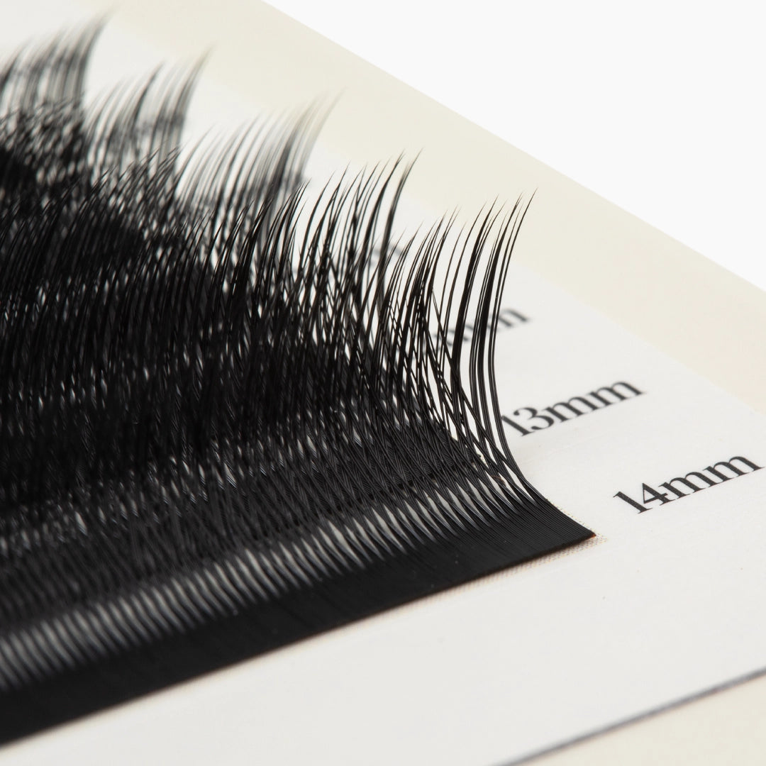 Macro close-up of black Kitten Lash extension fibres on a lash strip, showing the curl and length markings.
