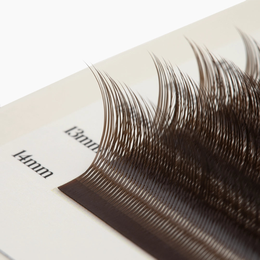 Macro close-up of brown Kitten Lash extension fibres on 13mm and 14mm strips, showing their upward curl and fine texture.