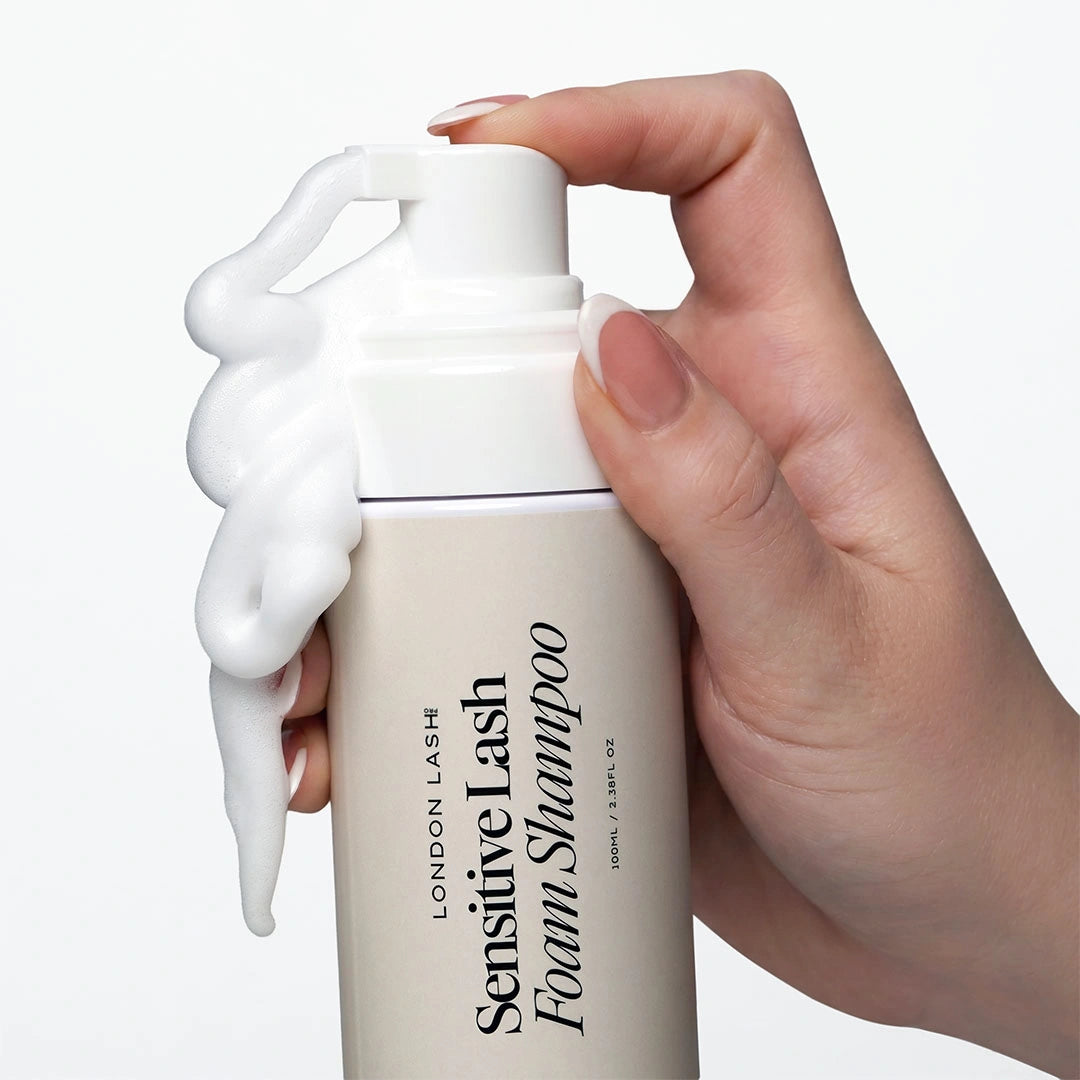 Close-up of a hand pressing the pump of the London Lash Sensitive Lash Foam Shampoo, dispensing rich cleansing foam from the bottle.